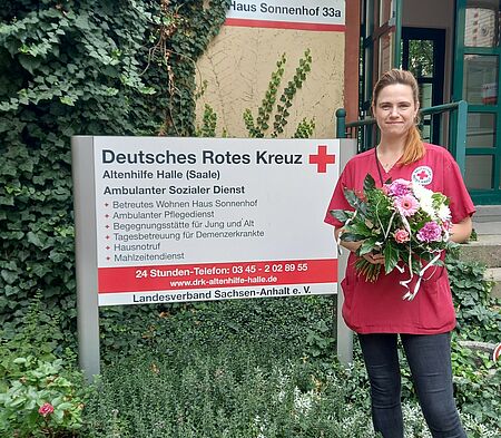 Pflegefachfrau steht mit Blumenstrauß in den Händen vor Haus Sonnenhof der DRK Altenhilfe Halle