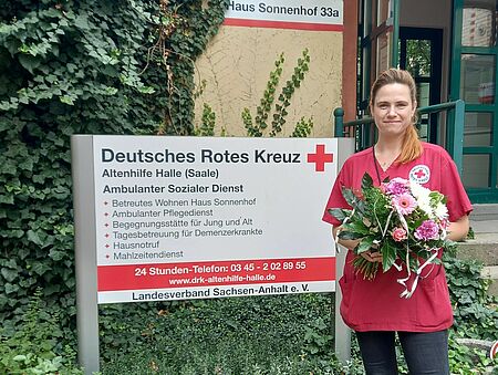 Pflegefachfrau steht mit Blumenstrauß in den Händen vor Haus Sonnenhof der DRK Altenhilfe Halle