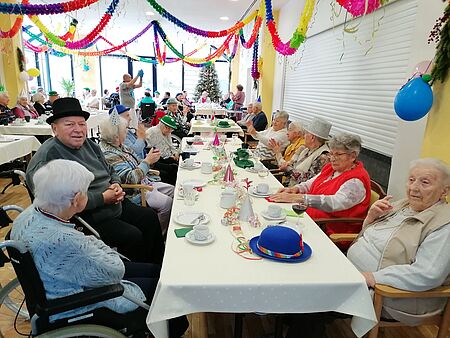 Seniorinnen und Senioren sitzen in geschmückten Raum an festlich gedeckter Tischreihe