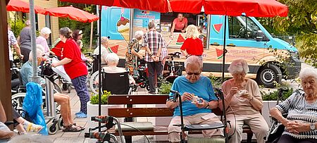 Im Hintergrund blaues Eismobil, im Vordergrund Seniorinnen und Senioren, die Eis essen