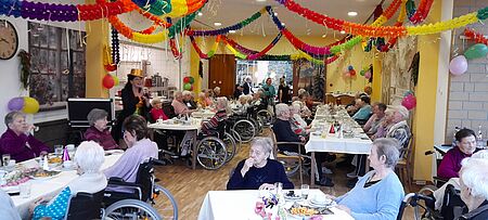 Festlich geschmückter Saal mit Seniorinnen und Senioren am mehreren Tischen