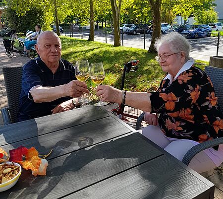 Seniorin und Senior sitzen am Tisch im Freien und stoßen mit Weinglas an