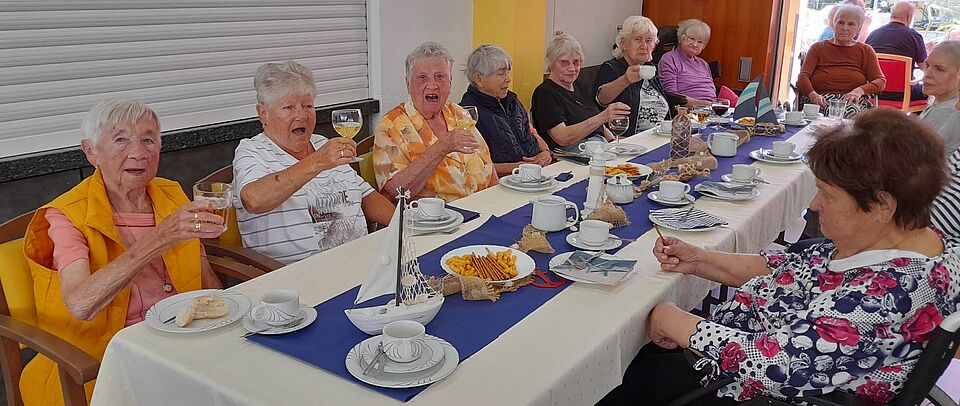 Seemannsfest Seniorinnen und Senioren sitzen um gedeckten Tisch herum und stoßen mit Gläsern an