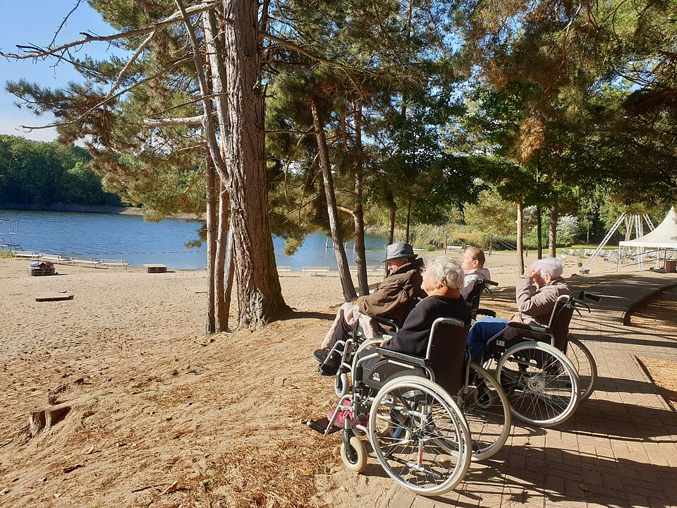 Ausflug Seniorinnen im Rollstuhl, im Hintergrund See mit Sandstrand