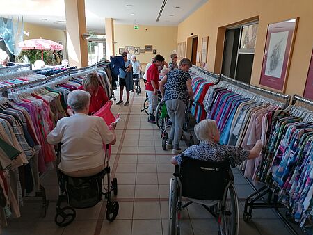 Seniorinnen stöbern durch Kleidung, die an Kleiderständern im Foyer hängt.