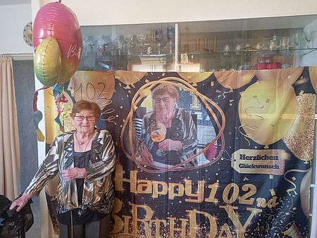 Seniorin vor Banner mit Aufschrift "Happy 102. Birthday"