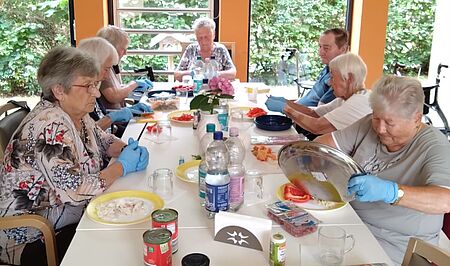 Seniorinnen und Senior schneiden an langer Tafel Gemüse für Pizza klein