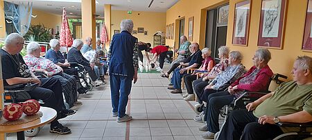Mehrere Bewohnerinnen und Bewohner des Altenpflegeheims und Gäste der Tagespflege sitzen um "Kegelbahn" herum und schauen zu