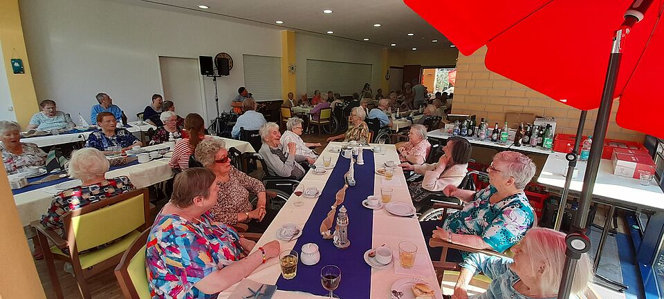 Seniorinnen und Senioren sitzen an langen Tafeln und unterhalten sich