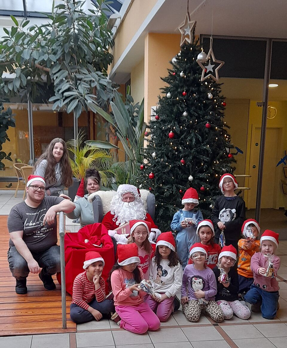 Kindergartenkinder mit Weihnachtsmann vor großem Tannenbaum
