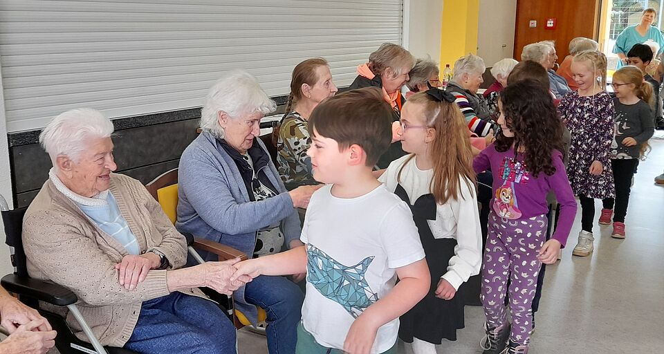 Kita-Kinder begrüßen Seniorinnen und Senioren, die in einer Reihe sitzen