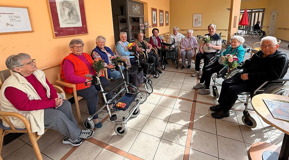 Vorbereitungen Heimbeiratswahl Seniorinnen und Senioren sitzen im Halbkreis auf Stühlen, einige halten Blumensträuße in den Händen
