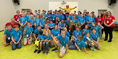 Gruppe aus Kindern, Jugendlichen und Betreuern in blauen und roten T-Shirts schauen in Kamera