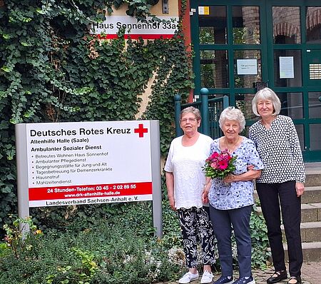 3 Frauen stehen vor Gebäude "Haus Sonnenhof", die Frau in der Mitte hält Blumenstrauß in der Hand
