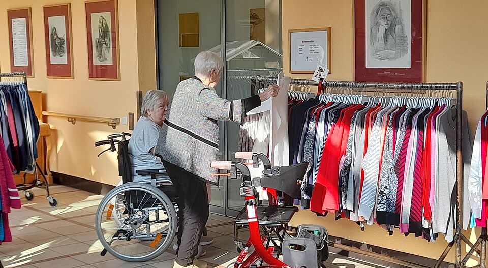 Seniorinnen stöbern durch Kleidung, die an Kleiderstange aufgehängt sind