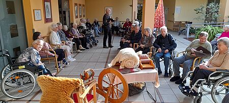 Seniorinnen und Senioren sitzen im Kreis um Spinnrad herum