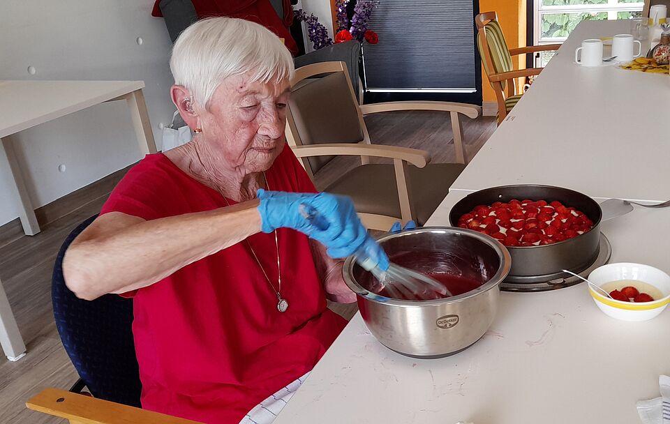 Erdbeerzeit Seniorin in rotem Oberteil rührt mit Schneebesen in Schüssel