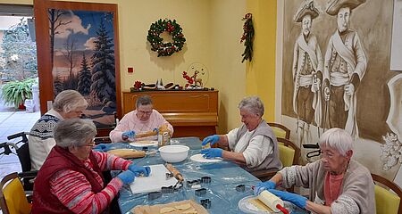 Seniorinnen sitzen um Tisch verteilt, rollen Teig aus und stechen Teig mit Formen aus