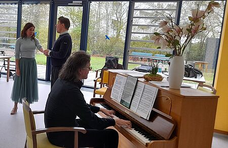 Mann am Klavier im Vordergrund, im Hintergrund Mann und Frau singend