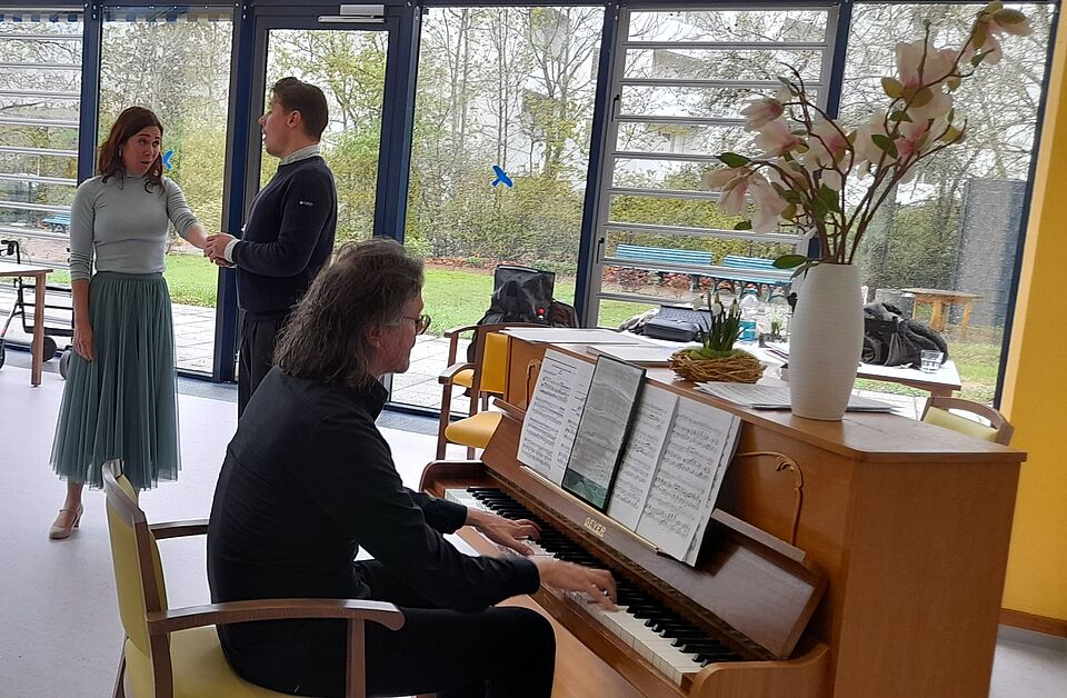 Mann am Klavier im Vordergrund, im Hintergrund Mann und Frau singend