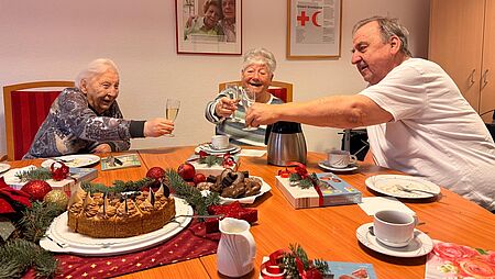 Zwei Frauen und ein Mann sitzen am Tisch und stoßen mit Gläsern an