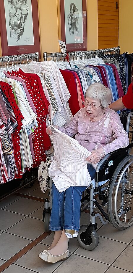 Seniorin in Rollstuhl stöbert durch Kleidung an Kleiderständer