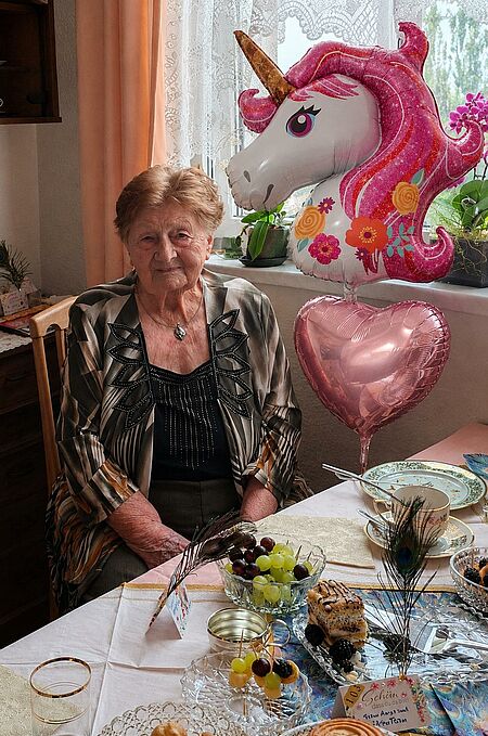 Seniorin sitzt an gedecktem Tisch mit zwei großen Luftballons im Hintergrund