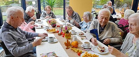 Seniorinnen und Senioren sitzen bei Kaffee und Kuchen um Tisch herum