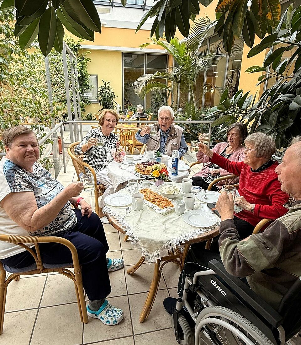 Seniorinnen und Senioren sitzen um Tisch mit Kaffee und Kuchen verteilt