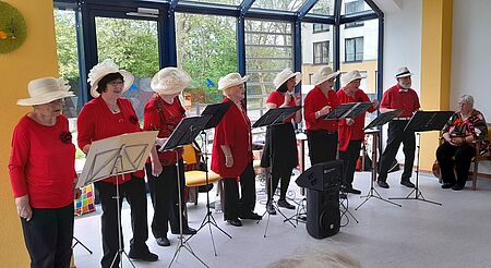 In Rot gekleidete Frauen stehen in einer Reihe vor Notenständern und singen